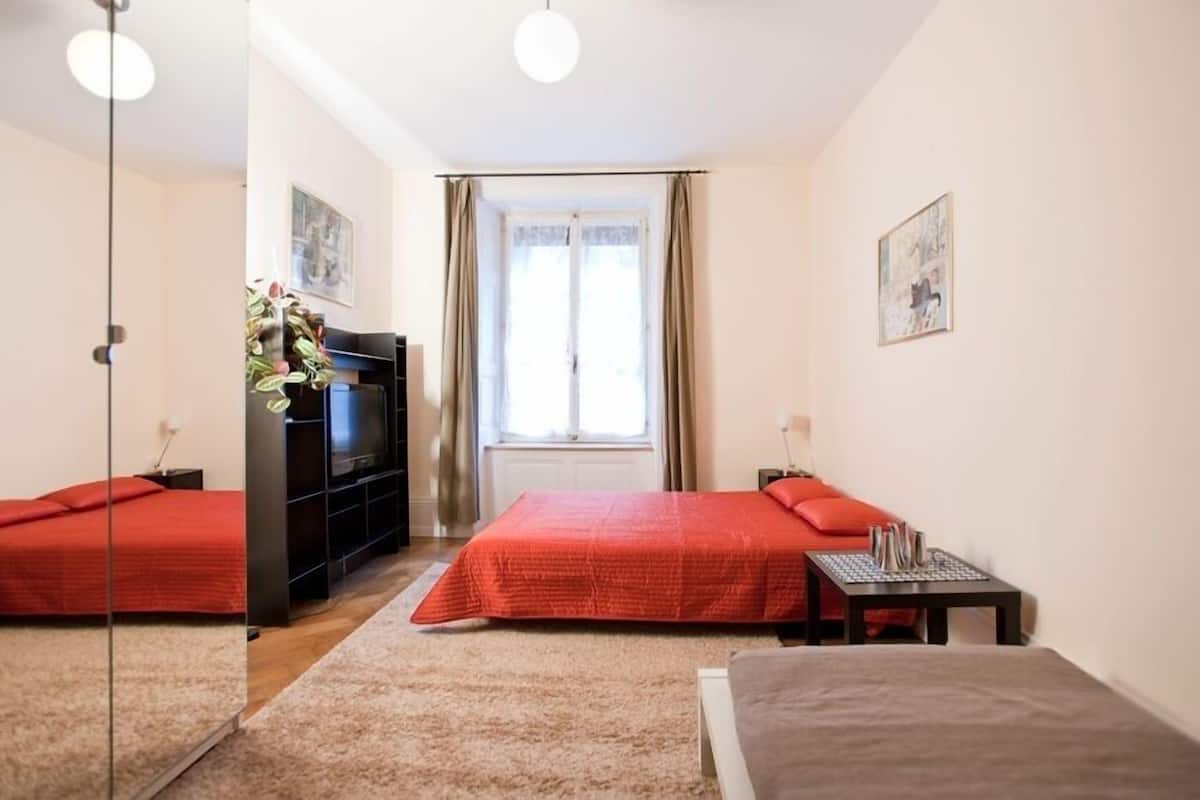 Un dormitorio con dos camas, un armario negro, una ventana con cortinas y una mesita con una lámpara.