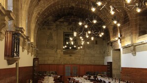 A banquet hall with high arched ceilings, wooden paneling, and chandeliers. Tables are set for dining.