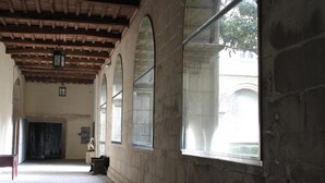 A corridor with stone walls, wooden ceiling beams, and large windows.