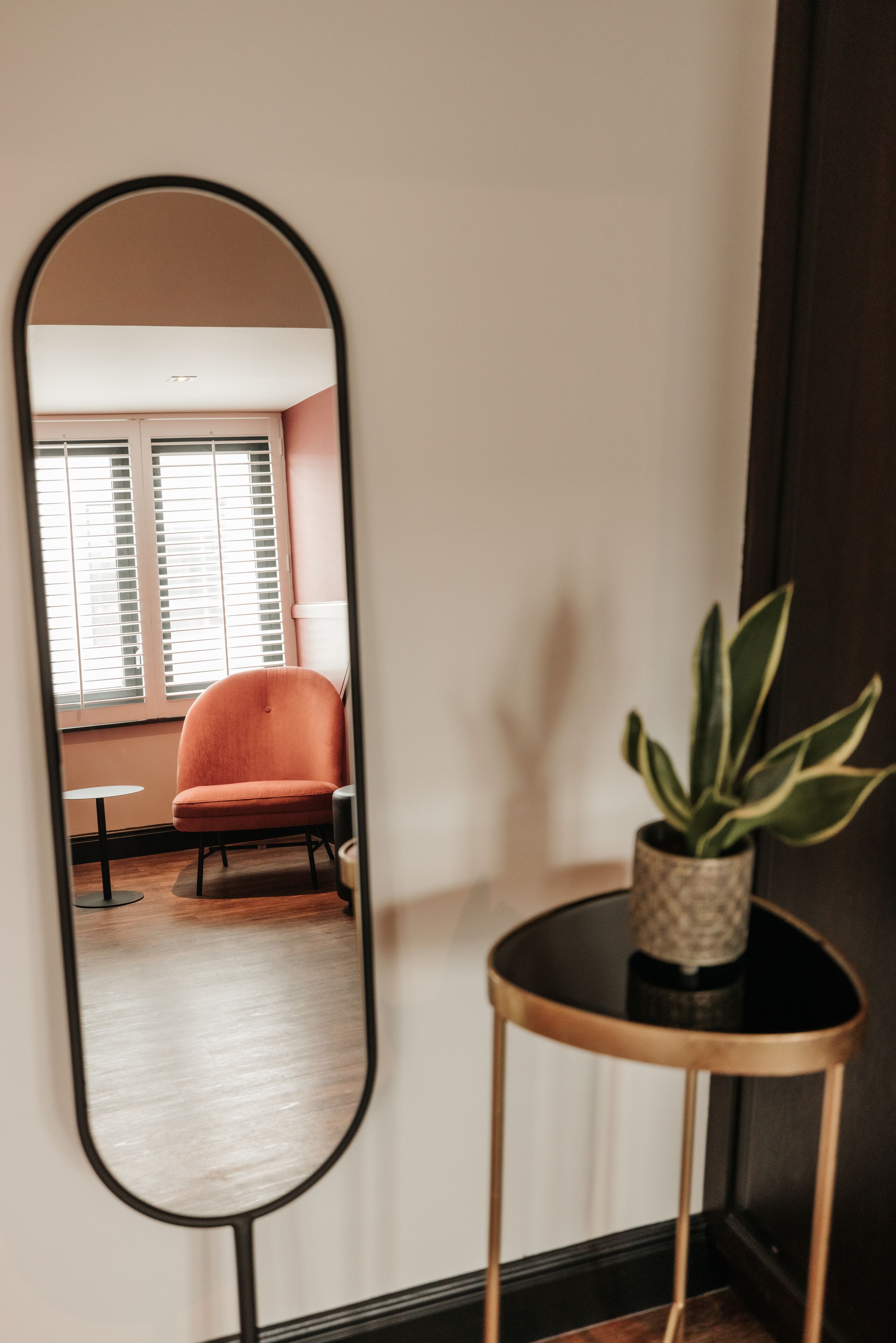 Une pièce avec un grand miroir qui reflète une chaise et une plante en pot.