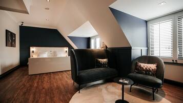 A modern living room with a dark blue accent wall, a sofa, a chair, a small coffee table, and a white console table with a lamp.