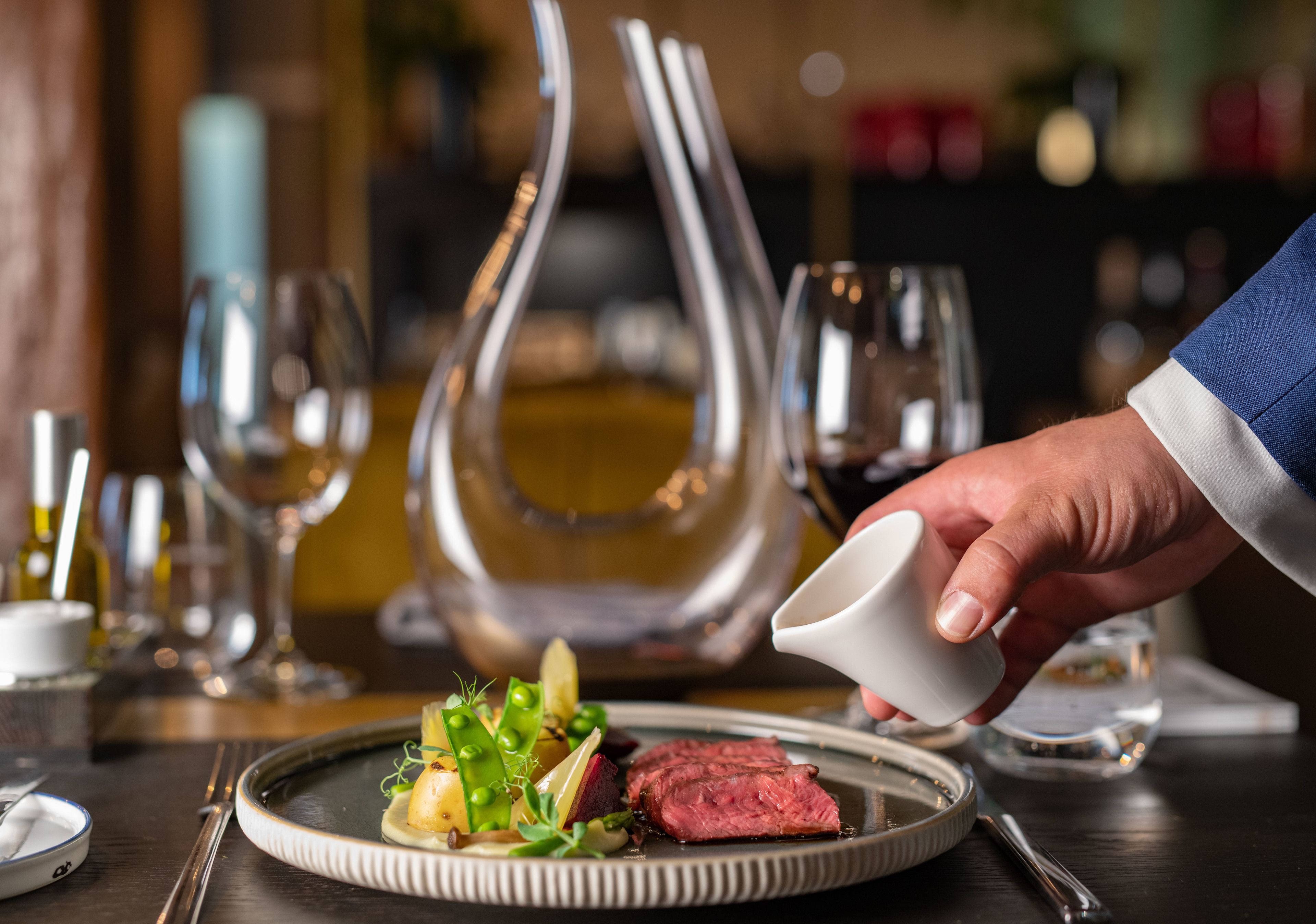A person pouring a liquid from a small white cup onto a plate with food.