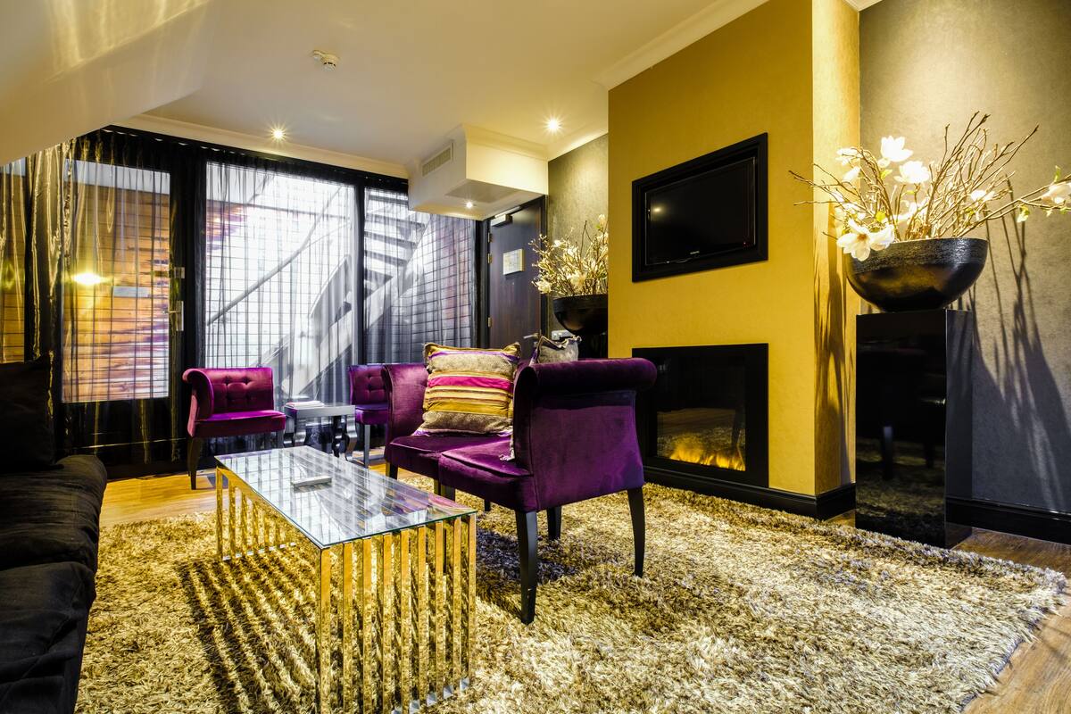 A modern living room with a fireplace, purple sofas, and a glass coffee table.