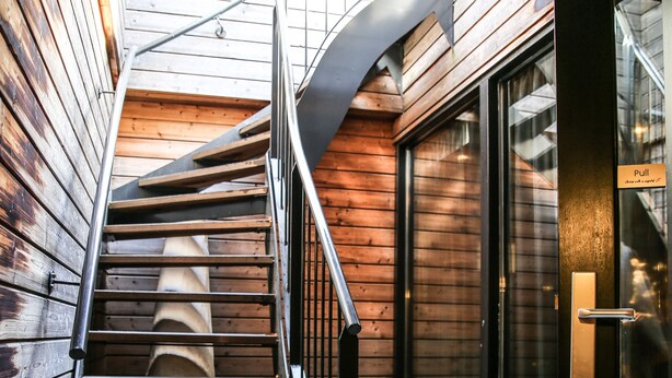 A spiral staircase with metal railings, wooden walls, and a glass door with a sign.