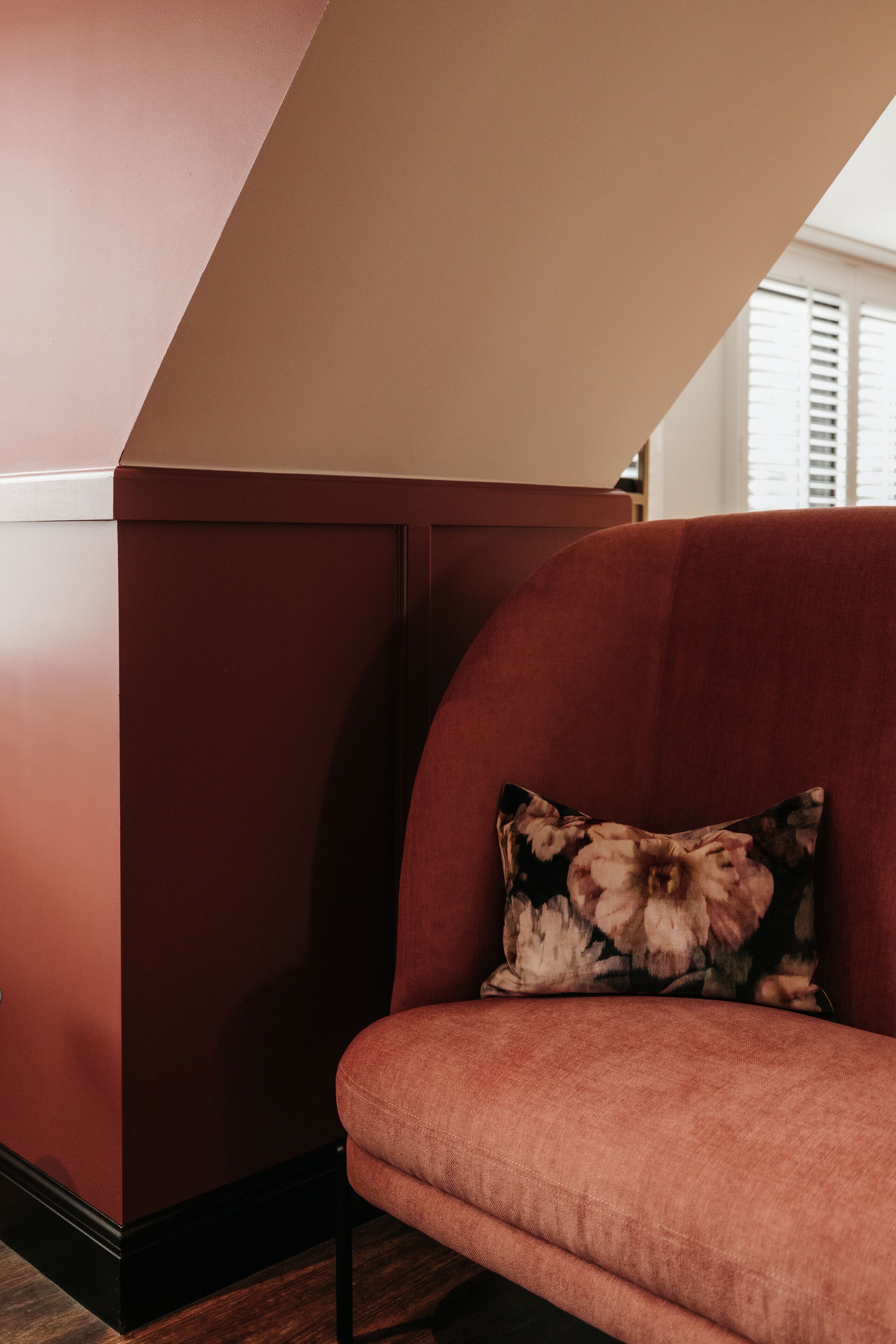 A corner of a room with a red wall and a red sofa with a floral pillow.