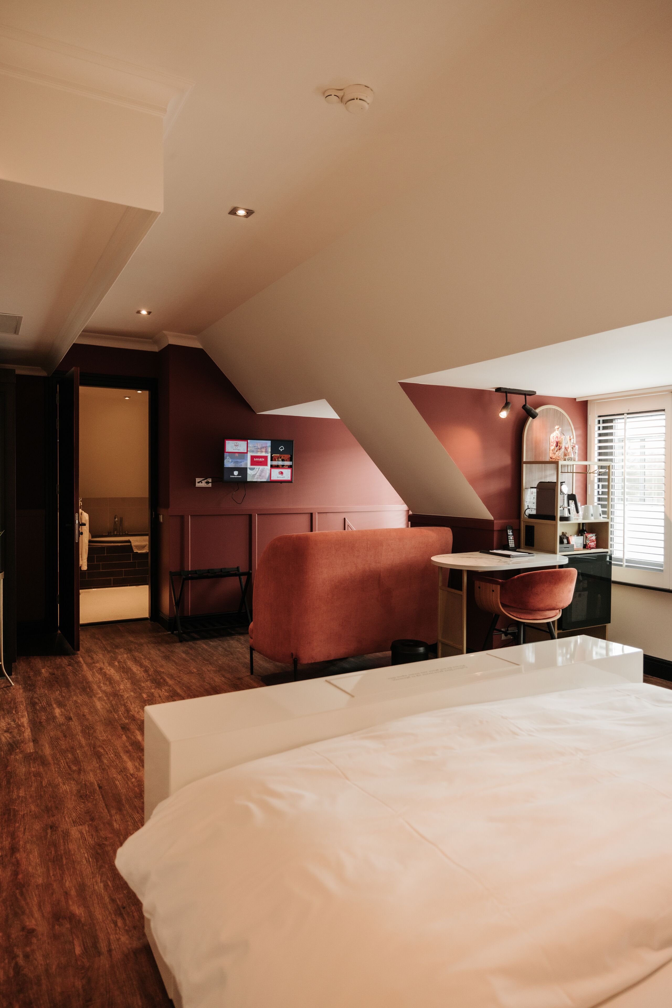 A hotel room with a bed, a desk, a chair, and a small seating area.
