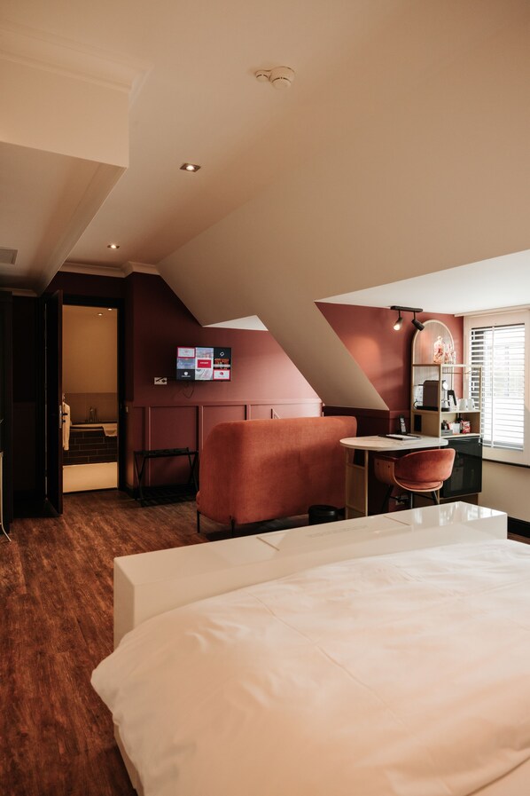 A hotel room with a bed, a desk, a chair, and a small seating area.