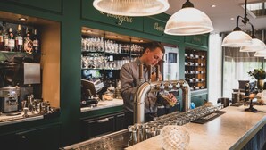 A bar area with a bartender preparing drinks, shelves with bottles, and a coffee machine.