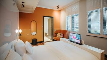 A modern hotel room with a large bed, a desk with a computer, and a window with blinds.