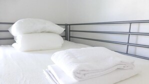 A neatly made bed with white linens and pillows, a metal headboard, and a plain white wall. - Acco Hostel (Stockholm)