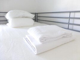 Una cama bien tendida con sábanas y almohadas blancas, cabecera de metal y pared blanca lisa.