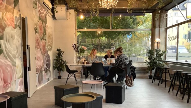 A modern cafe with a floral mural, round tables, and potted plants. - Acco Hostel (Stockholm)