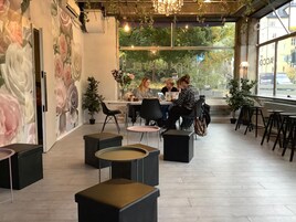 Un café moderno con un mural floral, mesas redondas y plantas en macetas.