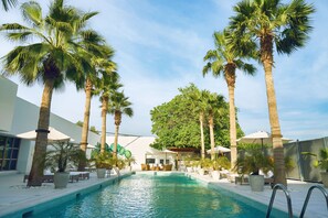 A pool area with palm trees, lounge chairs, and umbrellas. - Palmyard Hotel (Manama)
