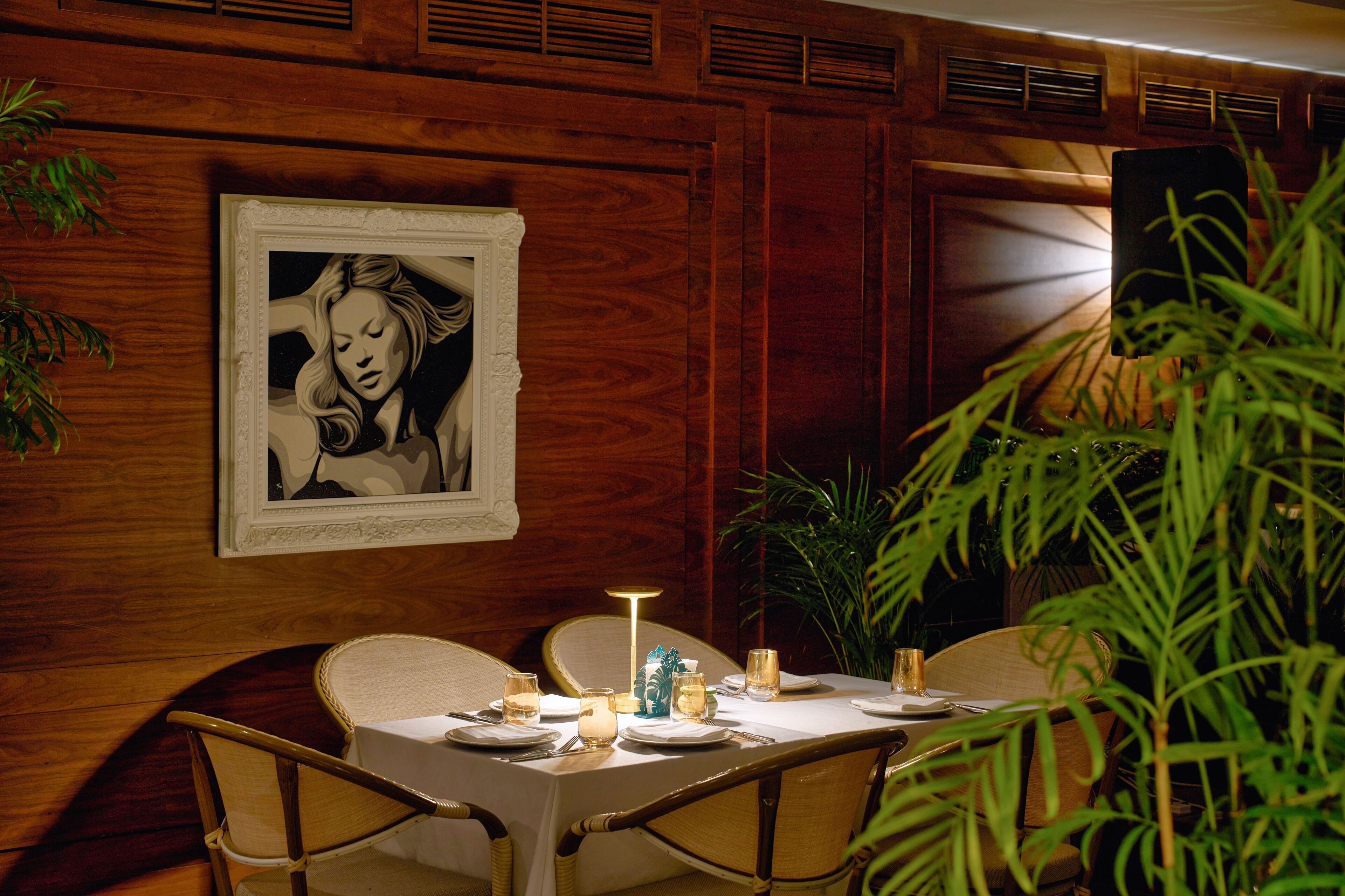 A dining area with a wooden wall, a framed artwork, and a table set with plates, glasses, and candles.