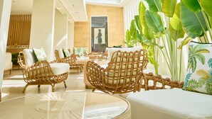 A spacious indoor area with a high ceiling and a glass roof, featuring wicker furniture and large green plants. - Palmyard Hotel (Manama)