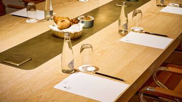 A conference table with documents, a basket of pastries, and glass bottles.