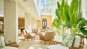A spacious lobby with wicker furniture, a glass ceiling, and large green plants. - Palmyard Hotel (Manama)