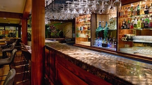 A bar area with a wooden counter, hanging wine glasses, and shelves of liquor bottles. - Palmyard Hotel (Manama)