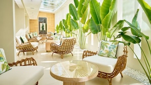 A spacious indoor area with wicker furniture, large windows, and tropical plants. - Palmyard Hotel (Manama)