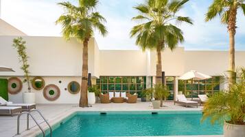 A poolside area with lounge chairs, a seating area, and palm trees.