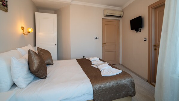 Habitación de hotel con cama, almohadas, un edredón, televisor montado en la pared y unidad de aire acondicionado.