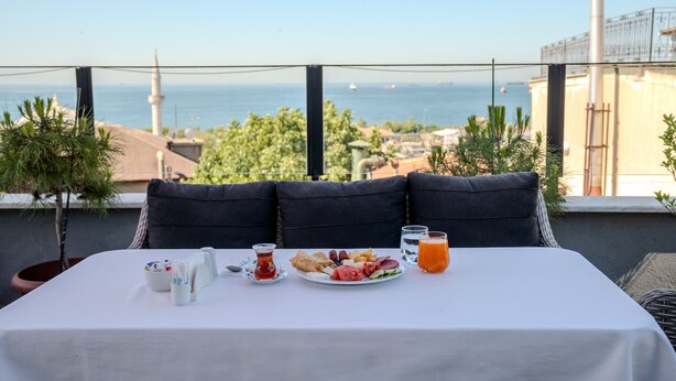 A dining table with a breakfast spread, a view of the sea, and a mosque in the background. - Sultanahmet Cesme Hotel (Istanbul)