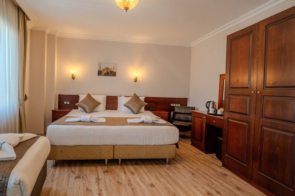 A hotel room with a large bed, wooden headboard, two bedside tables, a desk, and a wardrobe.