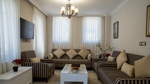 A living room with striped sofas, a white coffee table, and a TV mounted on the wall. - Sultanahmet Cesme Hotel (Istanbul)