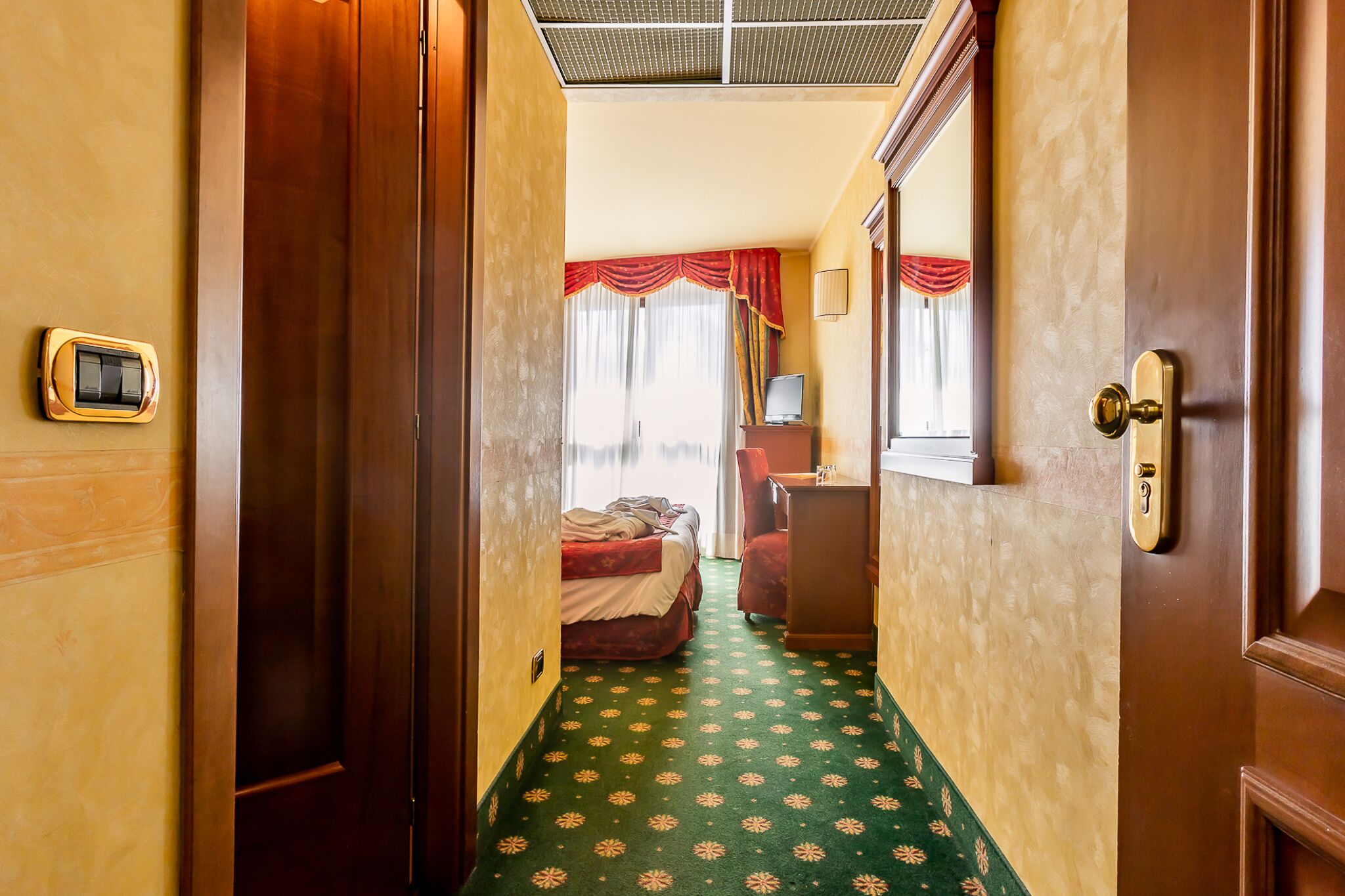 A hotel room with a bed, a desk, a chair, a television, and a window with curtains.