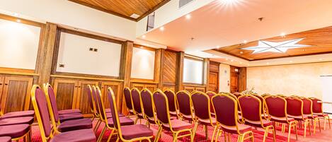 A conference room with rows of red chairs and a wooden ceiling.