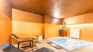 A spa area with a hot tub, seating, and a tiled wall. - Hotel Cristallo (Sestriere)