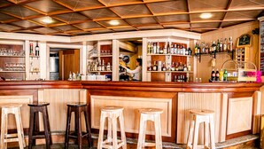 A bar area with wooden stools, shelves of bottles, and a bartender preparing drinks. - Hotel Cristallo (Sestriere)