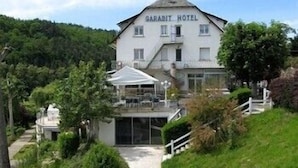 A white building labeled "GARABIT HOTEL" with a covered outdoor seating area and a pathway leading to the entrance. - Garabit Hôtel (Anglards-de-Saint-Flour)