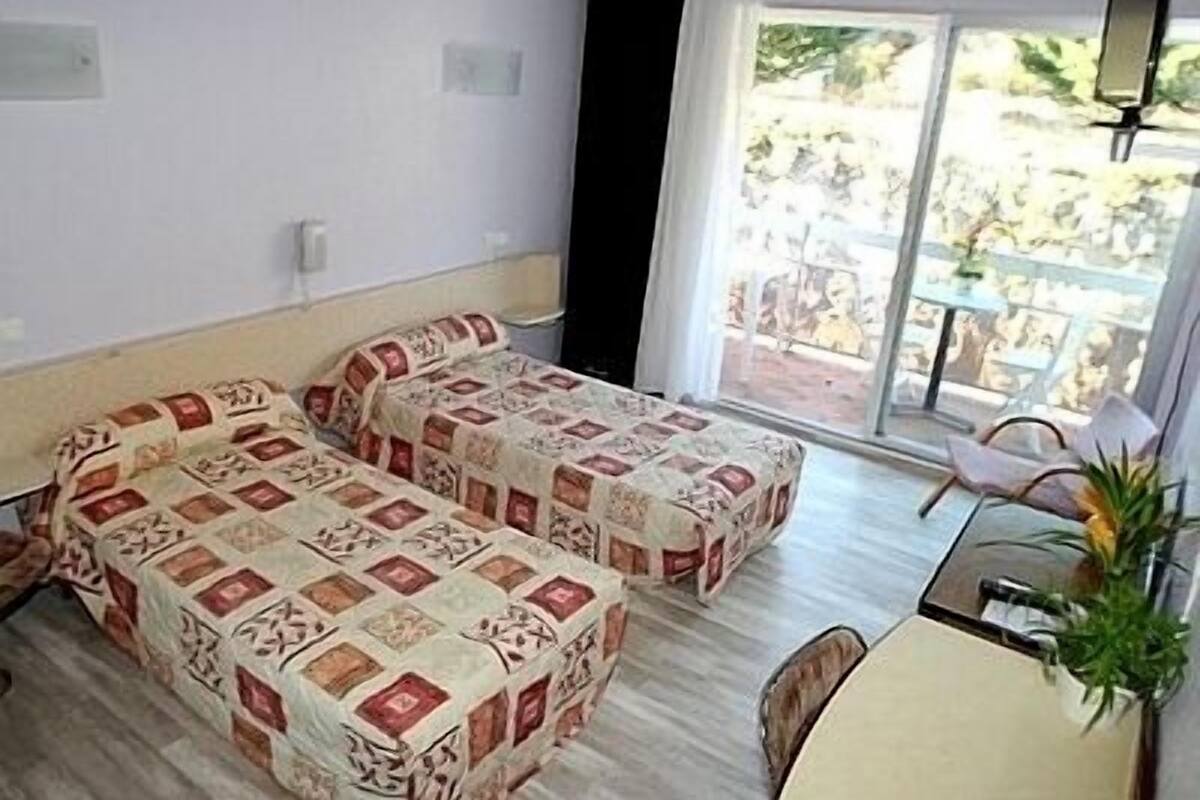 A room with two beds, a dining table, and a balcony with a table and chairs.