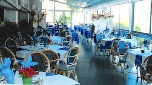 A restaurant with tables and chairs arranged in rows, large windows, and hanging decorations. - Garabit Hôtel (Anglards-de-Saint-Flour)