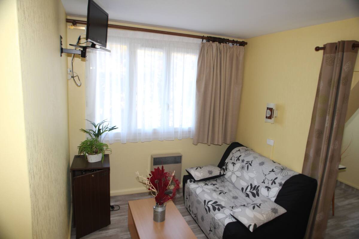 A living room with a sofa, a coffee table, a TV mounted on the wall, and a window with curtains.