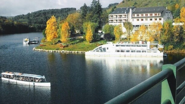 A river with a large white boat docked near a building with multiple windows and balconies. - Garabit Hôtel (Anglards-de-Saint-Flour)