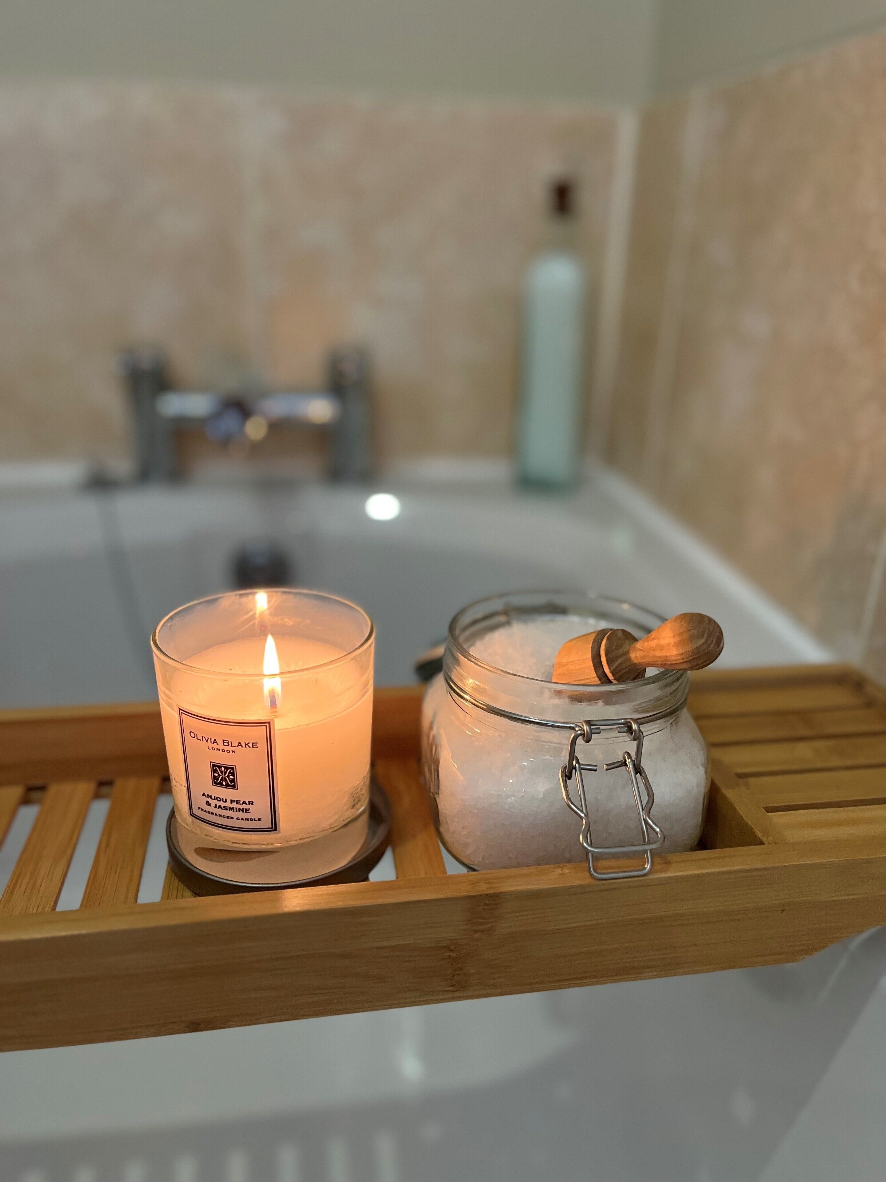 Un bagno con una candela accesa, un barattolo di sale e una bottiglia di sapone liquido su un vassoio di legno.