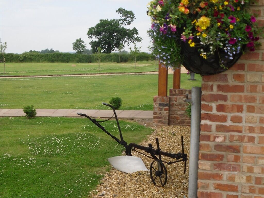 Un jardín con una bicicleta apoyada en una pared de ladrillo, una jardinera con flores y un campo de césped al fondo.