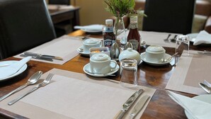 A dining table set with plates, cutlery, and condiments, with a lamp and window view in the background. - New Farm Bed & Breakfast (Winsford)