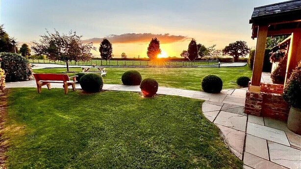 A well-maintained garden with a bench, a gazebo, and a clear view of the sunset over a body of water. - New Farm Bed & Breakfast (Winsford)