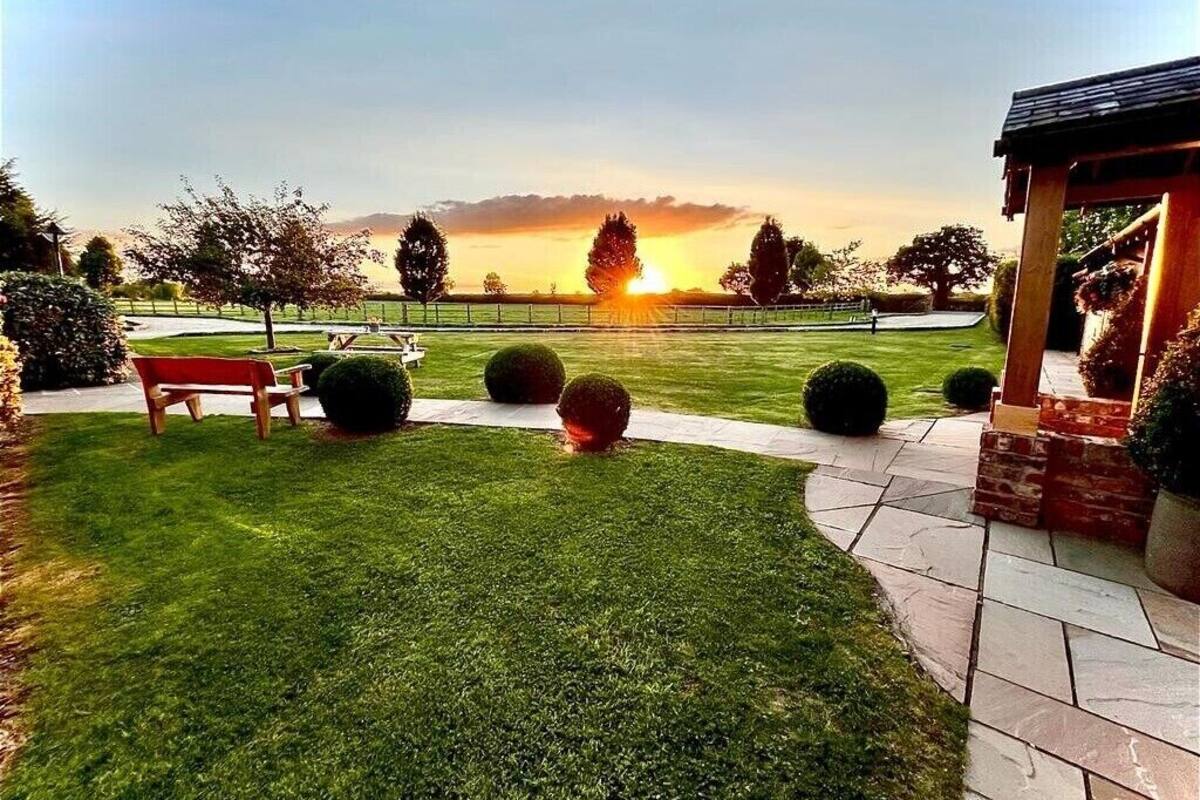 A well-maintained garden with a bench, a gazebo, and a clear view of the sunset over a body of water.