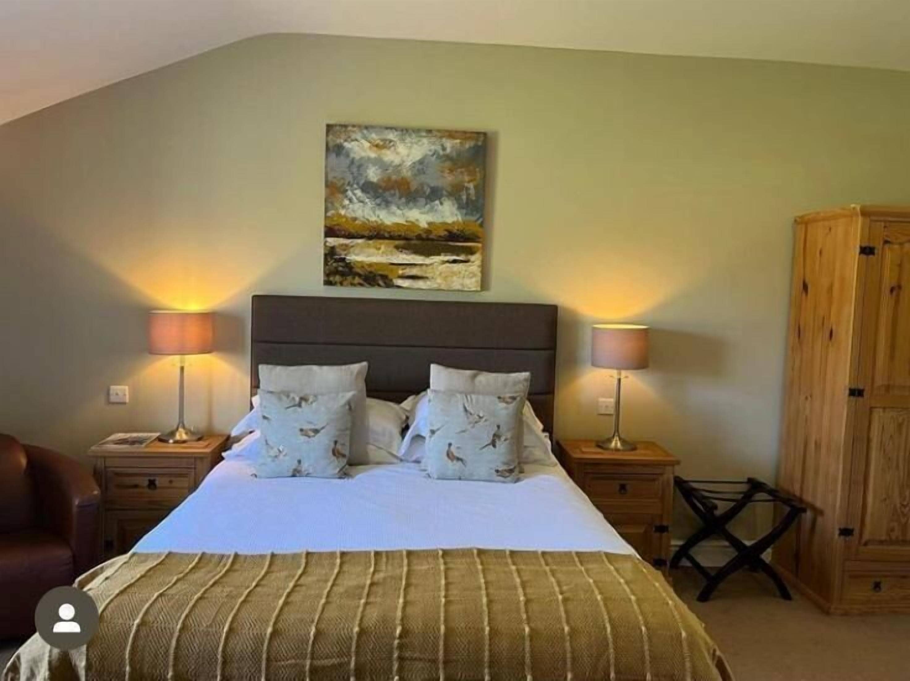 Une chambre à coucher avec un lit, deux lampes de chevet, une armoire en bois et un tableau accroché au mur.