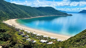 A coastal area with a beach, a row of houses, and lush green hills. - Six Senses Con Dao (Ho Chi Minh City)