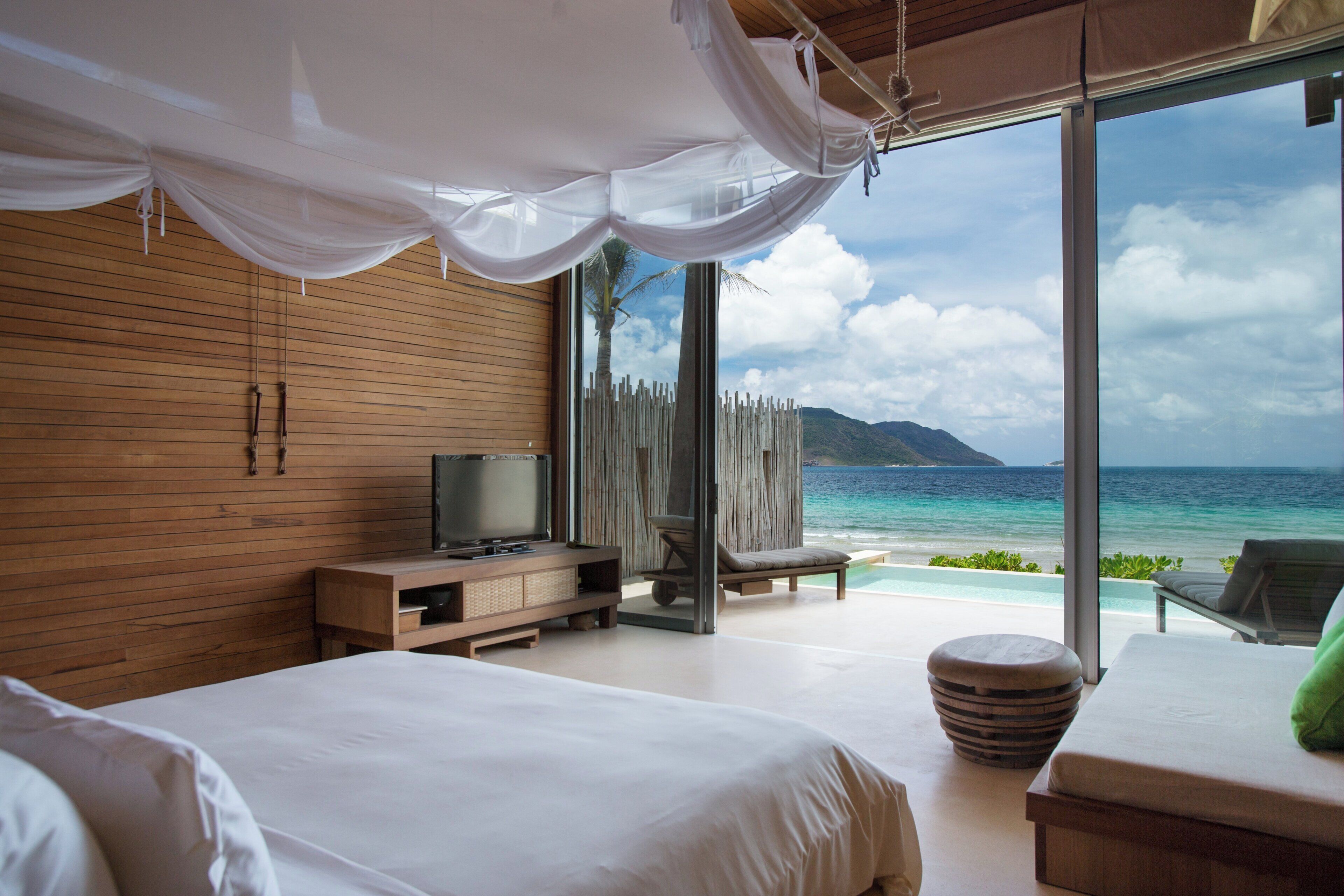 A bedroom with a large bed, a television, a wooden cabinet, and a view of the ocean.