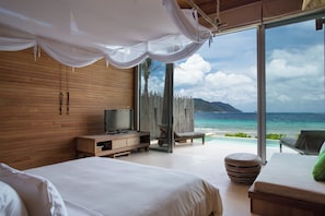 A bedroom with a large bed, a television, a wooden cabinet, and a view of the ocean. - Six Senses Con Dao (Ho Chi Minh City)