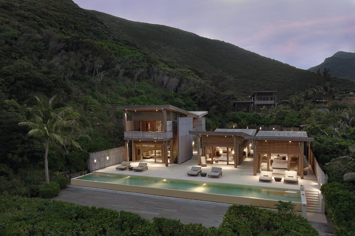 A modern two-story house with a swimming pool, surrounded by lush greenery and hills.