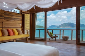 A bedroom with a large bed, a sofa, and a chair with a view of the sea and mountains. - Six Senses Con Dao (Ho Chi Minh City)