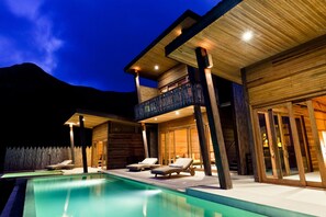 Un resort moderno con piscina, fachada de madera y un balcón con sillones de descanso.